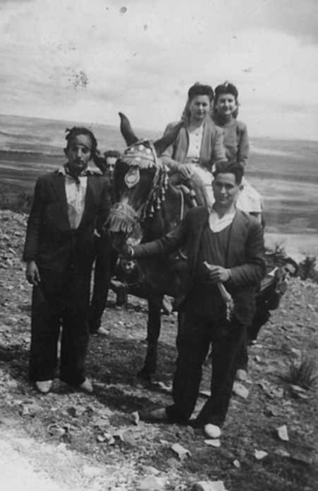 Dos mujeres subidas en un burro junto a dos hombres. Calamocha.