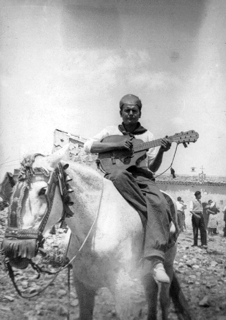 Hombre tocando una guitarra sobre un caballo. Con Santa BÃ¡rbara "la vieja" al fondo. Calamocha.