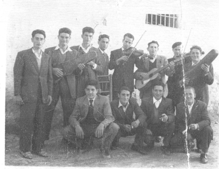 Grupo de hombres, algunos tocando instrumentos. Loscos.