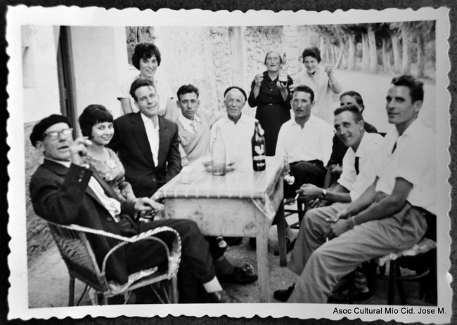 Grupo de hombres y mujeres de diferentes edades bebiendo en torno a una mesa en la calle