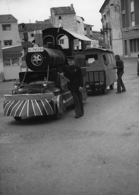 Varios hombres junto a una carroza con forma de locomotora en las calles de Calamocha.