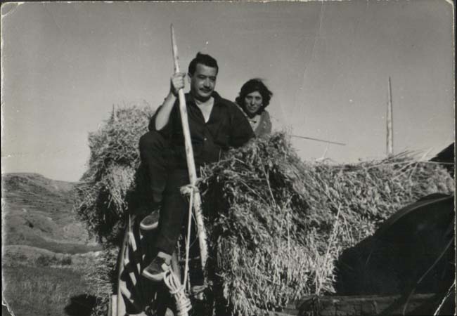 Hombre y mujer subidos a un carro lleno de paja